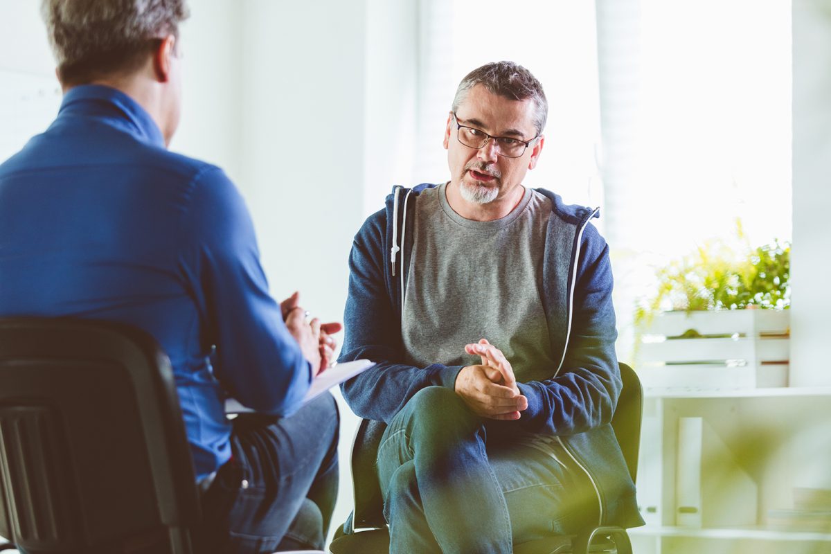 Mature psychotherapist talking with depressed man. Coach is discussing about mental illness with man. They are in meeting in psychotherapeutic office